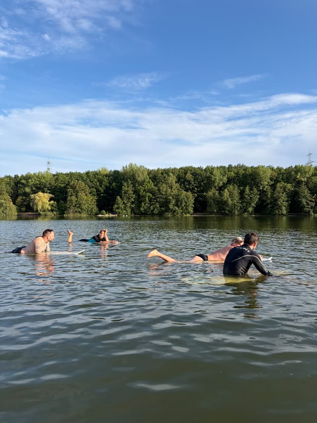 Vier Menschen liegen auf ihren Boards, Sommerhimmel über dem See