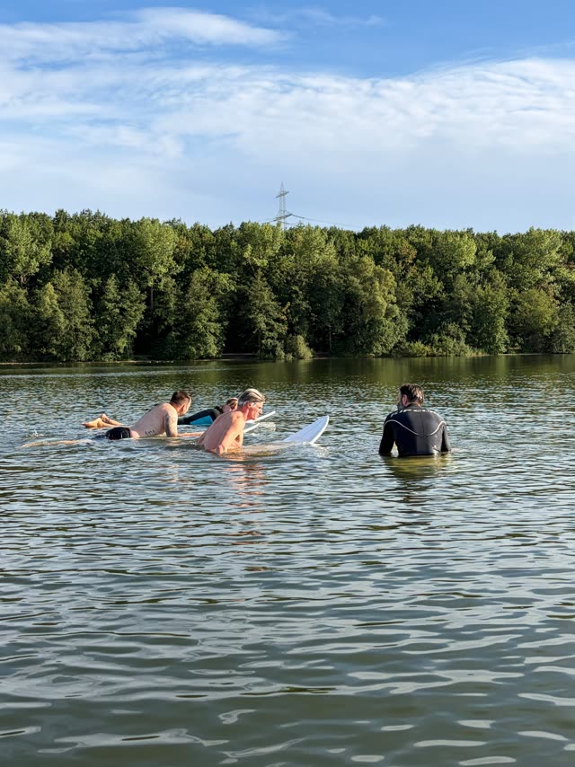 Gruppe auf Boards im Wasser, blauer Himmel über dem Waldufer