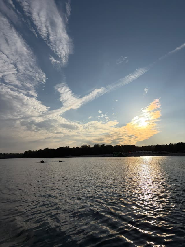 Weiter Blick über den See bei Sonnenuntergang, zwei Paddler auf dem Wasser